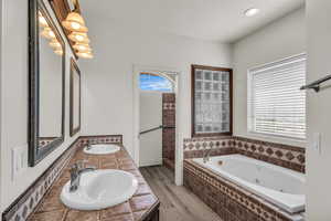 Bathroom featuring wood finished floors, a jetted tub, double vanity, and recessed lighting