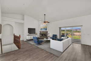 Living area with a ceiling fan, wood finished floors, a high end fireplace, and lofted ceiling