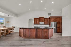 Kitchen featuring recessed lighting, freestanding refrigerator, a large island, a chandelier, and arched walkways