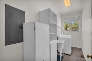 Washroom with independent washer and dryer, electric panel, wood finished floors, and a textured ceiling