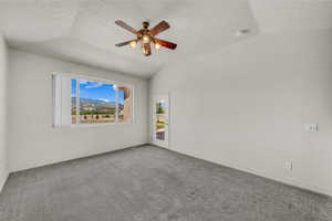 Carpeted empty room featuring vaulted ceiling, a textured ceiling, a ceiling fan, and a mountain view