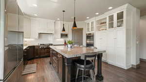Kitchen with stainless steel appliances, dark brown cabinetry, white cabinets, a breakfast bar, and recessed lighting