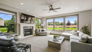Living room with a fireplace, a textured ceiling, carpet floors, a ceiling fan, and recessed lighting