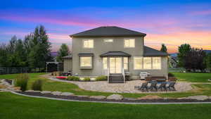 Back of property at dusk with a shingled roof, a patio area, and stucco siding