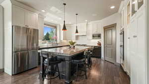 Kitchen with appliances with stainless steel finishes, a center island, dark wood-style flooring, recessed lighting, and a breakfast bar area