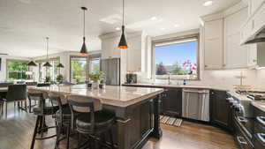 Kitchen with decorative backsplash, stainless steel appliances, light stone countertops, a textured ceiling, and range hood