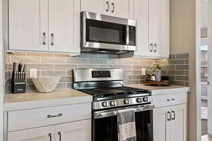 Kitchen with range with gas stovetop, stainless steel microwave, light countertops, white cabinets, and decorative backsplash