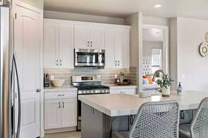 Kitchen featuring backsplash, stainless steel appliances, a kitchen breakfast bar, white cabinetry, and light countertops