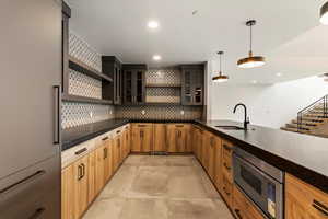 Kitchen with open shelves, backsplash, dark countertops, glass insert cabinets, and recessed lighting