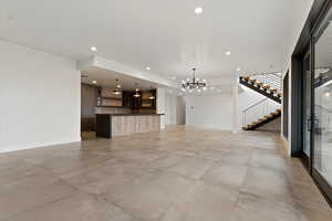 Unfurnished living room with a chandelier, stairs, recessed lighting, and concrete floors