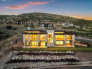 Back of house at dusk featuring a balcony, a mountain view, and a lawn