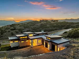 Back of house at dusk featuring a mountain view, stone siding, an attached garage, a metal roof
