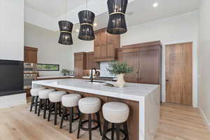 Kitchen with modern cabinets, a large island with sink, light wood-style flooring, hanging light fixtures, and a towering ceiling