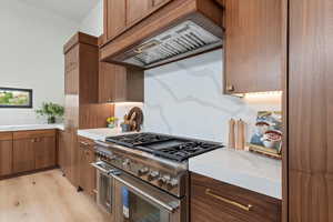 Kitchen featuring range with two ovens, custom exhaust hood, light wood finished floors, and tasteful backsplash