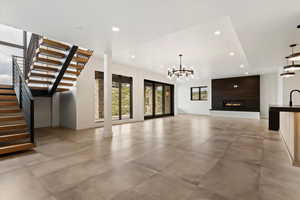 Unfurnished living room with stairway, a chandelier, recessed lighting, a fireplace, and concrete flooring