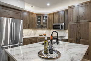 Kitchen featuring stainless steel appliances, tasteful backsplash, glass insert cabinets, and light stone countertops