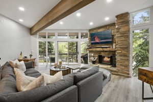 Living room with wood finished floors, beamed ceiling, a stone fireplace, recessed lighting, and plenty of natural light