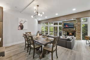 Dining room featuring healthy amount of natural light, a stone fireplace, light wood-style flooring, recessed lighting, and a chandelier