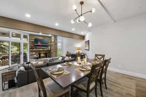 Dining space with beamed ceiling, a stone fireplace, light wood-style floors, recessed lighting, and a chandelier