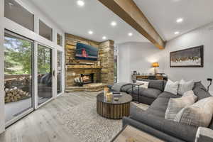 Living area with beam ceiling, wood finished floors, recessed lighting, and a stone fireplace
