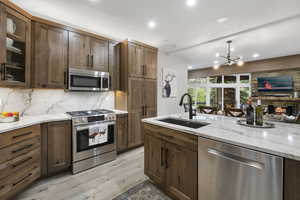 Kitchen with appliances with stainless steel finishes, backsplash, light wood-type flooring, glass insert cabinets, and a chandelier