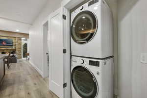 Laundry Area with stacked full size washer / dryer and light wood-style flooring