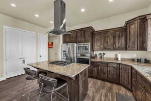 Kitchen with island exhaust hood, appliances with stainless steel finishes, a kitchen island, a kitchen bar, and dark brown cabinets