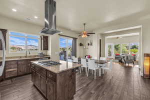 Kitchen featuring ceiling fan, island exhaust hood, dark wood finished floors, dark brown cabinets, and light stone counters