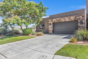 View of front of property featuring stone siding, driveway, an attached garage, and a front lawn