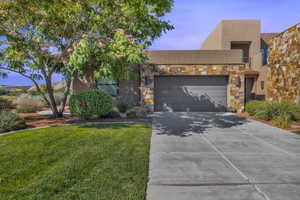 View of front of property with an attached garage, driveway, a front yard, stone siding, and stucco siding