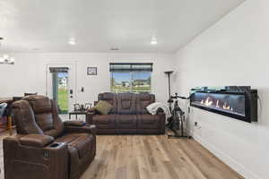 Living room with healthy amount of natural light, light wood-style flooring, a chandelier, a textured ceiling, and a glass covered fireplace