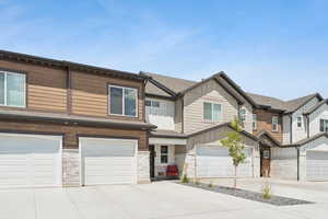 View of front of home with board and batten siding, a garage, driveway, and stone siding