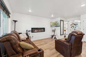 Living room with light wood-style floors, a glass covered fireplace, and recessed lighting