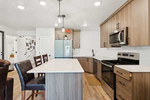 Kitchen featuring stainless steel appliances, a breakfast bar area, light wood finished floors, open floor plan, and decorative backsplash