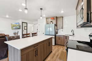 Kitchen featuring electric stove, freestanding refrigerator, light wood-style floors, stainless steel microwave, and tasteful backsplash