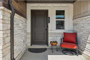 View of exterior entry featuring stone siding and a porch