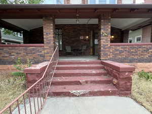 Doorway to property with covered porch and brick siding