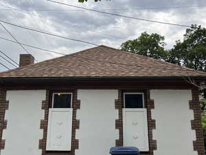 View of front of property featuring a shingled roof, a chimney, and brick siding