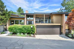 View of front of home with driveway, an attached garage, a chimney, a balcony, and brick siding