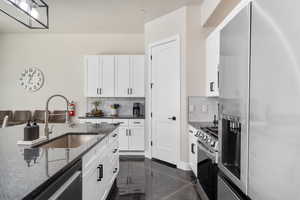 Kitchen with stainless steel appliances, white cabinetry, dark stone counters, and backsplash