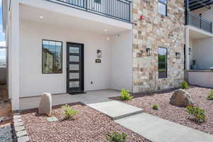 Property entrance with a balcony, stone siding, and stucco siding