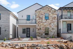 View of front of home featuring a balcony, stone siding, and stucco siding