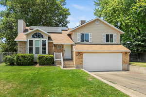 Tri-level home with a chimney, roof mounted solar panels, driveway, a garage, and brick siding