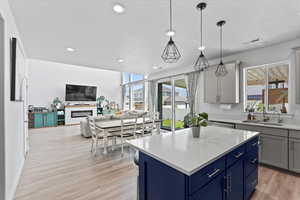 Kitchen featuring a center island, light wood-style floors, blue cabinetry, a fireplace, and decorative light fixtures