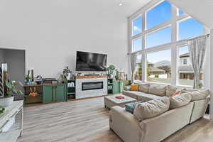 Living area with light wood-type flooring, a towering ceiling, and a glass covered fireplace