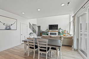 Dining area with light wood finished floors, a glass covered fireplace, and recessed lighting