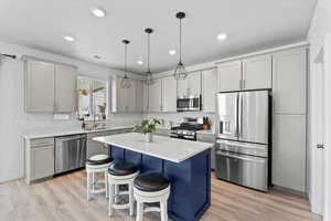 Kitchen featuring appliances with stainless steel finishes, light countertops, a center island, a kitchen bar, and hanging light fixtures