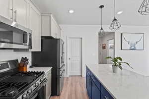 Kitchen with stainless steel appliances, blue cabinets, white cabinets, light wood-style floors, and light stone counters