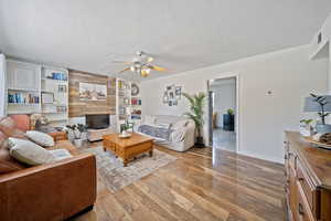 Living area with built in shelves, wood finished floors, a ceiling fan, and a textured ceiling