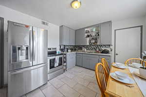 Kitchen featuring gray cabinetry, appliances with stainless steel finishes, open shelves, tasteful backsplash, and light tile patterned flooring